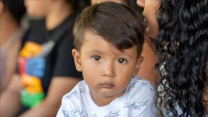 Un niño mira fijamente a la cámara sentado con un adulto.