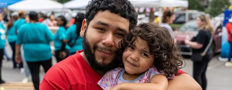 Un hombre y su hija abrazados al aire libre en un evento